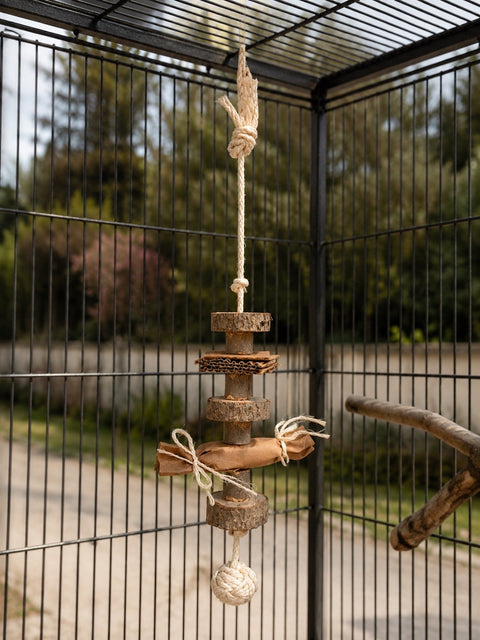 Juguete colgante natural para loros de laurel con cartón, papel kraft y cuerda de sisal colocado en una voladera.